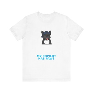 May include: A white short-sleeved t-shirt featuring a graphic of a black French bulldog wearing a blue baseball cap with its tongue out. Below the dog, the text reads MY COPILOT HAS PAWS in bold blue capital letters centred on the chest.