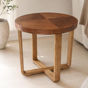 Può includere: Un tavolino rotondo in legno con un piano marrone scuro caratterizzato da un motivo a venature diviso in quattro quadranti. La base è composta da quattro gambe verticali collegate da una struttura di supporto centrale a croce, in legno chiaro.