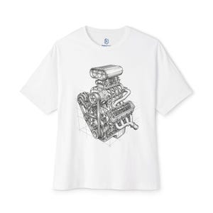 May include: A white short-sleeve t-shirt featuring a detailed black and white line art illustration of a supercharged V8 engine on the front. The graphic includes a blower, pulleys, belts, and exhaust headers set against a subtle grid background.