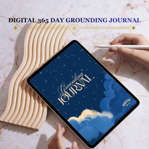 以下が含まれることがあります： デジタルタブレットには、星空と雲が描かれたダークブルーの表紙に「Grounding Journal」と「Noetic Planner」の文字が表示されています。タブレットの横には、大理石模様の表面に置かれた、明るい色で波打つ質感のオブジェクトがあります。