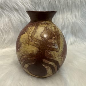 Może przedstawiać: Okrągły ceramiczny wazon z ciemnobrązową szyjką i kulistym korpusem o dwukolorowym wykończeniu. Powierzchnia ma nakrapianą kremowo-brązową fakturę z wyraźną, ciemnobrązową wypukłą grafiką przedstawiającą mrówkę umieszczoną na froncie.