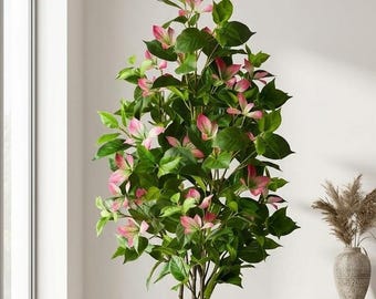 May include: A tall artificial tree with dark green leaves and variegated pink and green foliage. The plant is housed in a cylindrical dark gray textured pot, positioned next to a matching empty pot on a light-colored floor in a bright room.