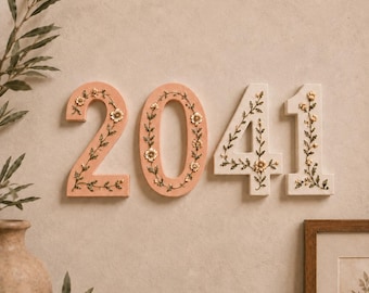 May include: The numbers 2, 0, 4, and 1 displayed as wall decor. The numbers 2 and 0 are a soft peach color, while 4 and 1 are off-white. Each number features a raised, intricate floral vine pattern with small white flowers and green leaves.