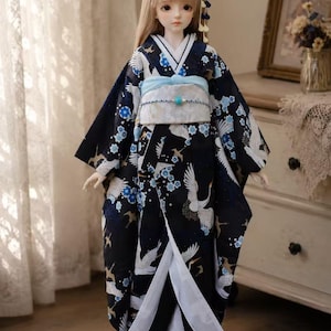 May include: A ball-jointed doll with long blonde hair wearing a black kimono featuring white crane and blue flower patterns. The outfit includes a light blue obi sash with a central turquoise bead, a white under-layer, and a small floral hair accessory.