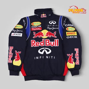 May include: A dark navy blue zip-up jacket featuring Red Bull branding, two red bulls, and Infiniti logos. The garment includes sponsor patches for Rauch, Geox, Total, Pepe Jeans, FXDD, Casio, and Pirelli, with blue and red side panel accents.