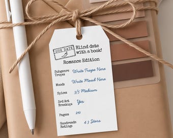 Puede incluir: Una etiqueta de papel rectangular blanca atada con cordel marrón a un paquete envuelto en color canela. La etiqueta presenta texto negro que dice "DUE DATE Blind date with a book! Romance Edition" y texto azul estilo manuscrito.