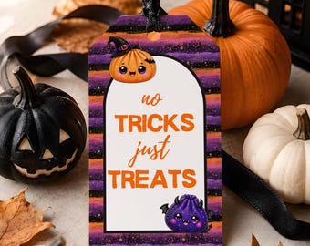 Puede incluir: Una etiqueta de regalo rectangular con una cinta negra, con un fondo de rayas moradas y naranjas con detalles brillantes. El arco blanco central muestra el texto naranja 'no TRICKS just TREATS' junto a una pequeña calabaza y una criatura morada.