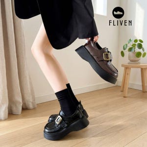 May include: A pair of black platform loafers with a thick sole and a metallic buckle detail across the top. The shoes are worn with black socks. The image includes the text FLIVEN with a shoe icon above it, indicating the brand name and logo.