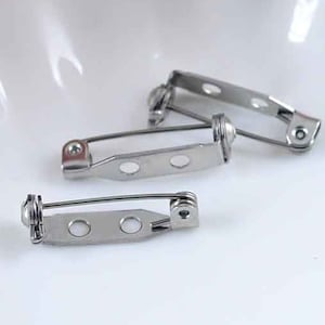 Puede incluir: Tres alfileres de broche de metal plateado con cierre de resorte. Los alfileres están diseñados para sujetar tela u otros materiales a la ropa u otros artículos.