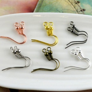 Könnte beinhalten: Sechs Paar Ohrhaken mit einer Feder und einer Kugel oben. Die Haken sind in Silber, Gold, Roségold und Schwarz erhältlich.