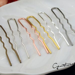 May include: Seven wavy hair pins in different metallic colors: gold, silver, rose gold, and bronze. The pins are arranged in a row on a white surface.