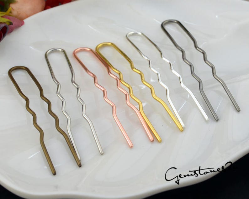 May include: Seven wavy hair pins in different metallic colors: gold, silver, rose gold, and bronze. The pins are arranged in a row on a white surface.