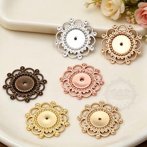 May include: A collection of ornate, filigree metal jewelry findings in various metallic finishes, including silver, gold, bronze, and rose gold. Each piece features a central circular setting, perfect for embellishments. The decorative elements are arranged in a floral pattern.