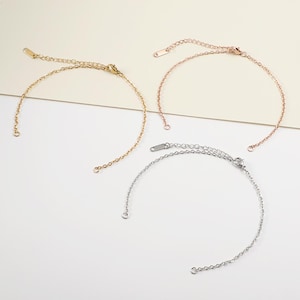 May include: Three delicate chain bracelets in gold, rose gold, and silver. Each bracelet features a fine chain with an adjustable length and a small clasp. The bracelets are displayed on a light background, showcasing their simple elegance.