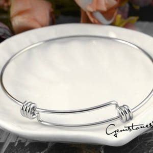 May include: A silver expandable bangle bracelet with a simple design. The bracelet has a spring-loaded clasp that allows it to fit a variety of wrist sizes.