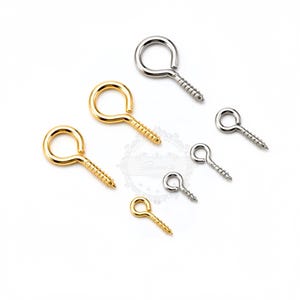 Può includere: Un assortimento di ganci a vite ad occhiello in tonalità oro e argento. I ganci hanno una parte superiore ad anello e una base a vite filettata. Le dimensioni variano, alcune sono piccole e altre più grandi. Questi sono probabilmente usati per l'artigianato o per appendere oggetti.
