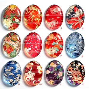 Op de afbeelding: Twaalf ovale glazen cabochons gerangschikt in een raster, elk met verschillende op Japan geïnspireerde patronen, waaronder bloemmotieven, kersenbloesems, golven en geometrische ontwerpen in levendige rode, blauwe, zwarte en paarse kleurenpaletten.
