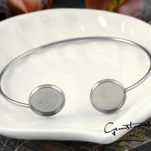 Puede incluir: Un brazalete de plata con dos engastes redondos de plata. El brazalete está abierto y listo para ser usado.