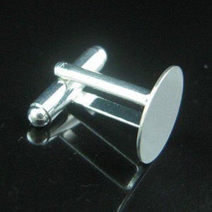 Può includere: Un singolo gemello d'argento con un perno cilindrico arrotondato e un retro di forma ovale. Il gemello è molto riflettente, con una finitura lucida, su uno sfondo scuro e lucido.