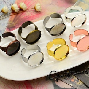 May include: Six adjustable ring blanks with round glass cabochon settings. The rings are made of metal in various finishes, including silver, gold, copper, and rose gold.