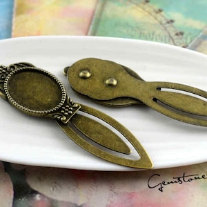 Può includere: Due ciondoli per segnalibri in bronzo antico. Uno ha una cornice rotonda e decorata con un centro vuoto. L'altro è un design semplice a forma di foglia.