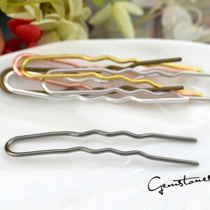 May include: A set of five wavy hair pins in different metallic colors: gold, rose gold, silver, and black. The pins are arranged in a row on a white surface.