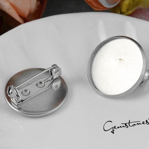 May include: Two silver-toned metal round brooch bases with a pin and catch closure. The bases are blank and ready to be decorated.