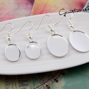 May include: Four silver earring blanks with round, oval-shaped settings. The settings are smooth and have a slightly raised edge. The earring hooks are simple and straight.