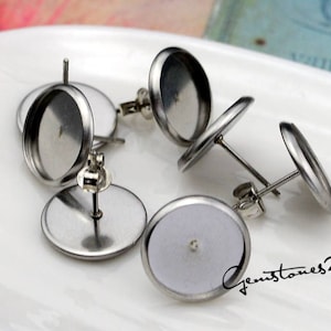 Op de afbeelding: Vijf zilveren oorbelbevestigingen met ronde, platte, zilveren bases en pinnen. De bases zijn ontworpen om een ronde, platte, glazen of plastic cabochon te houden.