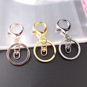 Pode incluir: Três chaveiros com diferentes acabamentos metálicos: dourado, prateado e ouro rosa. Cada chaveiro tem um anel circular e um fecho giratório.