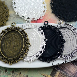 Puede incluir: Una colecci&oacute;n de bandejas colgantes ovaladas con bordes de filigrana ornamentados. El conjunto incluye cuatro engastes de metal en acabados bronce antiguo, plata y negro, cada uno con un &aacute;rea central rebajada y una anilla superior.