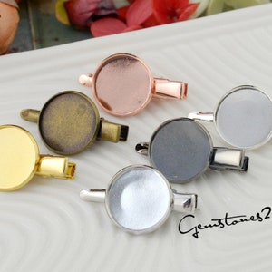 May include: Five round metal blanks for jewelry making, each with a different colored metal finish: gold, silver, bronze, black, and rose gold. Each blank is attached to a silver metal clip.