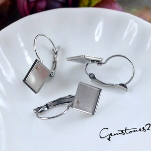 May include: Three silver earring blanks with square settings. The earring blanks are on a white surface.