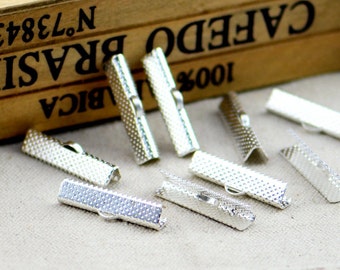 May include: Silver-colored metal clasps with a textured, dotted pattern. The clasps are rectangular with a small, curved hook on one side. The background includes a wooden box with the text "CAFEDO BRASIL".