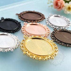 Puede incluir: Un conjunto de siete bandejas para colgantes ovaladas de metal con bordes de filigrana intrincados y bases interiores texturizadas. El set incluye varios acabados met&aacute;licos como oro, plata, oro rosa, negro y bronce, cada uno con una anilla.