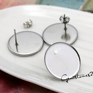 Op de afbeelding: Drie zilveren oorbelbevestigingen met een ronde, heldere glazen cabochon. De bevestigingen hebben een pen en een vlinder achterkant.