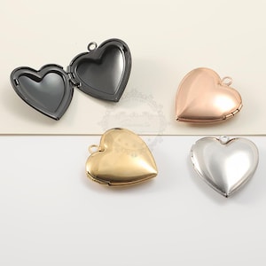 May include: Four heart-shaped lockets in different metallic finishes: black, rose gold, gold, and silver. One locket is open, revealing the interior. Each locket has a small loop for attaching to a chain or bracelet. The lockets are on a neutral background.