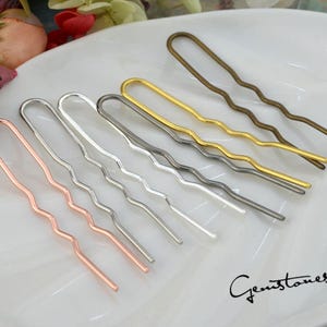 May include: A set of seven wavy hair pins in different metallic finishes, including gold, silver, bronze, and rose gold. The pins are arranged on a white surface.