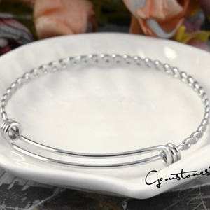 May include: A silver expandable bangle bracelet with a braided design. The bracelet is open and has a spring clasp.