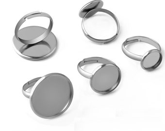 May include: Several silver-toned adjustable rings with a flat, round bezel. The rings are shown from various angles, highlighting their simple design and adjustable band. The bezels are ready for adding custom designs or embellishments.