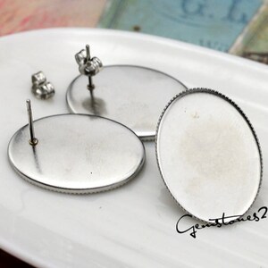 May include: Three silver oval-shaped earring settings with a post and a backing. The settings are on a white surface.