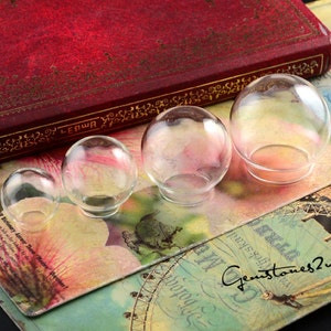 May include: Four clear glass dome shapes of varying sizes, arranged from largest to smallest on a colourful patterned surface. The domes are perfect for displaying small objects or creating miniature scenes.