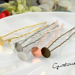 Pode incluir: Seis grampos de cabelo com cabeças redondas de metal em tons dourados, prateados e acobreados. Os grampos de cabelo estão dispostos sobre uma superfície branca.