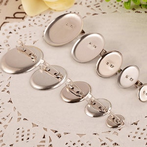 May include: A set of six silver-toned metal blank round and oval-shaped pin backings with attached pin backs. The pin backs are different sizes.