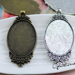 Könnte beinhalten: Zwei ovale Metall-Anhänger-Tabletts mit einem dekorativen Blumendesign. Die Tabletts sind silber- und bronzefarben und haben eine glatte, glänzende Oberfläche. Die Tabletts sind perfekt, um Schmuckherstellung eine persönliche Note zu verleihen.