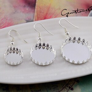 May include: Three silver earring settings with a crown design and a round, clear glass cabochon. The settings are different sizes.