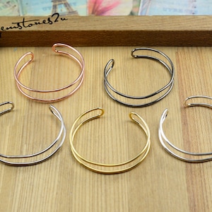 Op de afbeelding: Vijf dubbellaagse metalen armbanden in verschillende afwerkingen: rosé goud, zwart, zilver, goud en zilver. De armbanden worden getoond op een houten oppervlak.