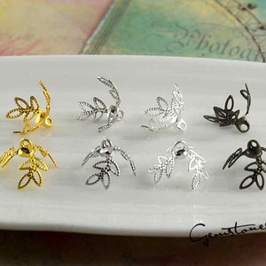 Op de afbeelding: Een assortiment blad-vormige sieraden onderdelen in goud, zilver en donker bronzen tinten. De onderdelen zijn gerangschikt op een wit oppervlak, waarbij hun delicate, opengewerkte ontwerpen worden getoond. De tekst "Gemstones2u" is inbegrepen.