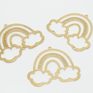 Könnte beinhalten: Drei goldene Regenbogen-Anhänger aus Metall mit Wolken. Jeder Anhänger hat ein ausgeschnittenes Design eines Regenbogens mit zwei Wolken.