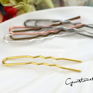 May include: A set of five gold, silver, and copper hair clips with a wavy design. The clips are arranged on a white surface.
